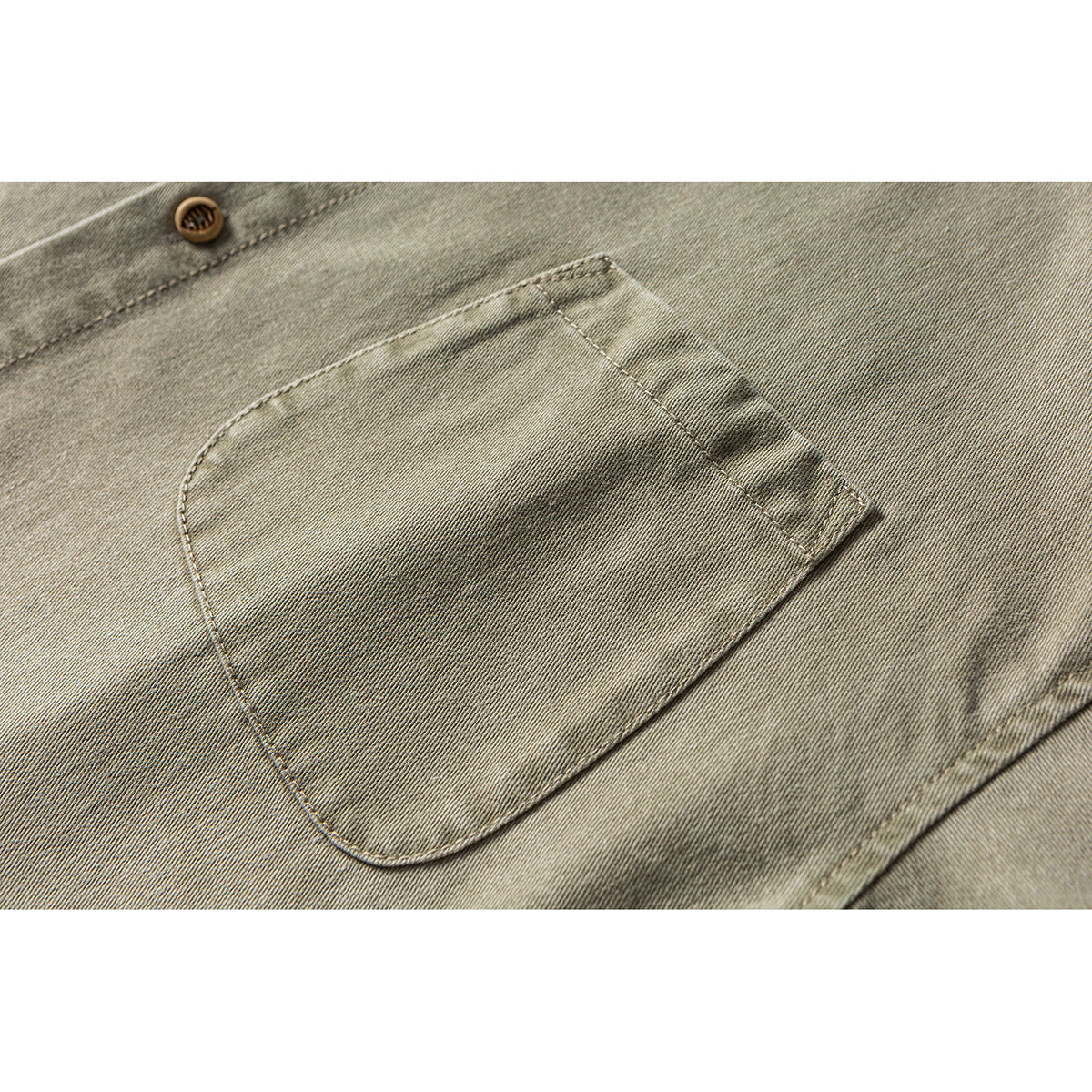 Close-up of a chest pocket on an olive-gray shirt, with a tan button visible above it.