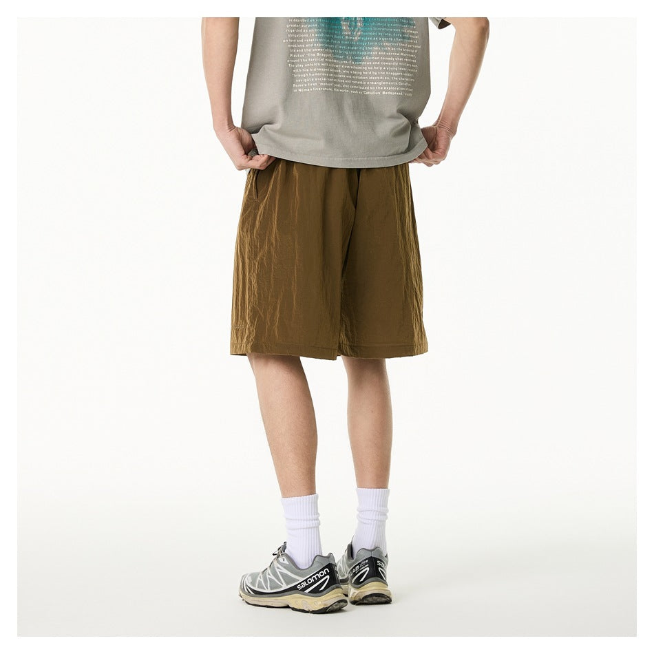 Rear view of a person wearing loose olive-brown shorts with a gray printed T-shirt, white socks, and sneakers.