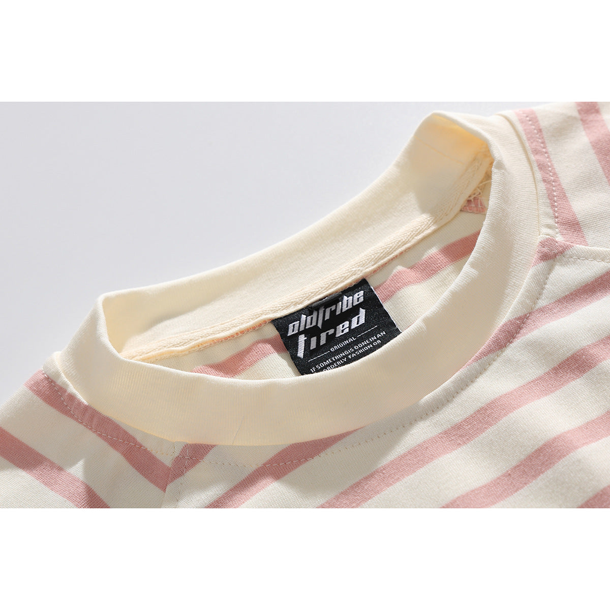 Close-up of a cream ribbed crew neckline and sewn black label on a cream T-shirt with dusty pink stripes.