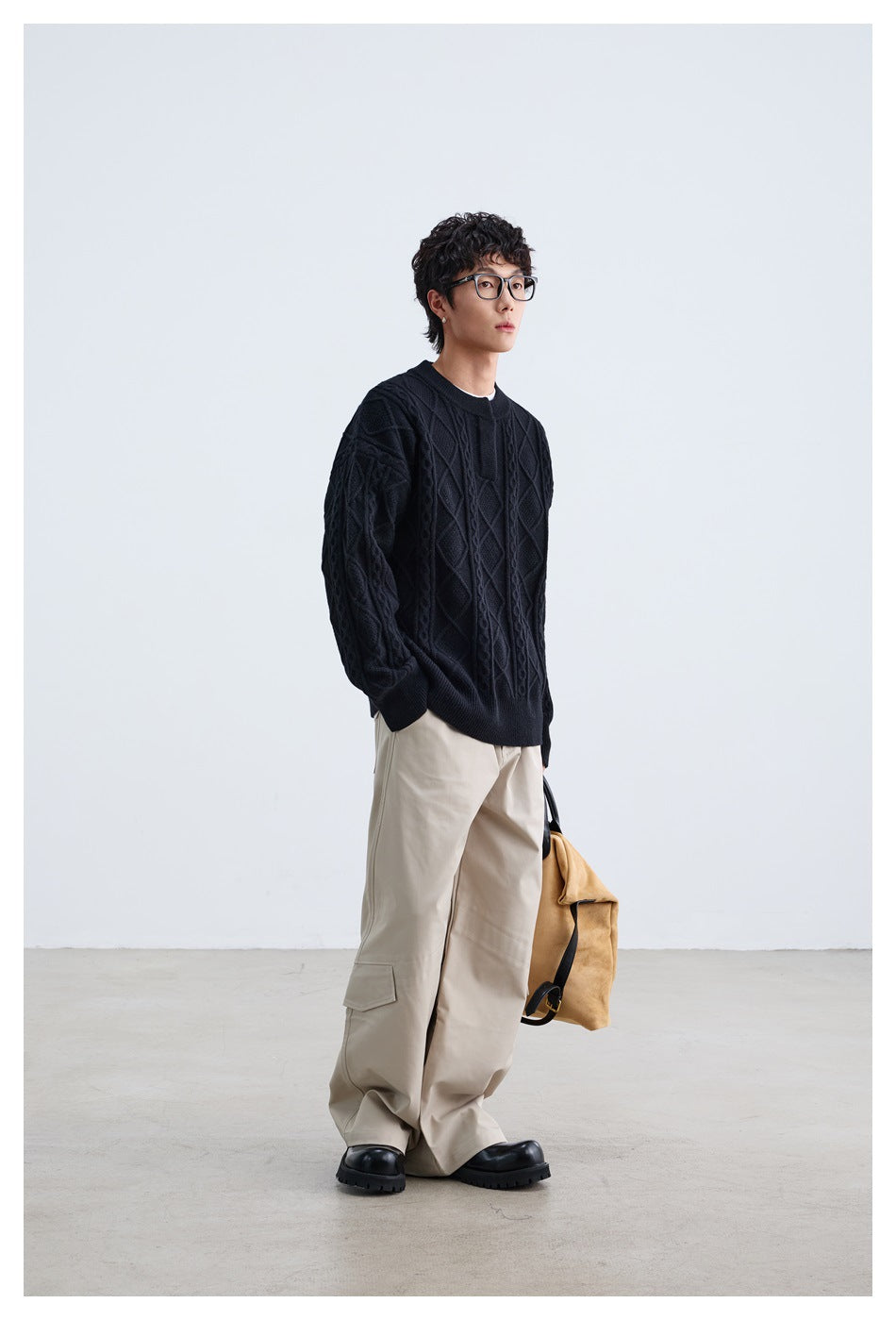 Full-length model in a black cable-knit sweater and loose beige trousers, carrying a tan bag.