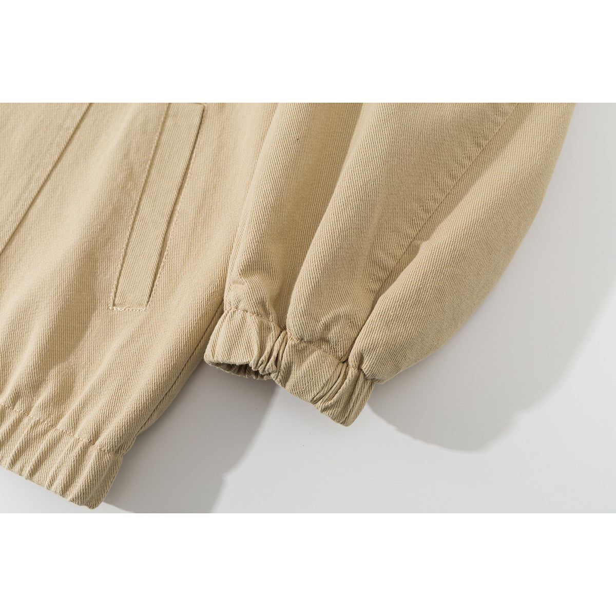 Close-up of a beige jacket sleeve with an elastic cuff and a slanted welt pocket.
