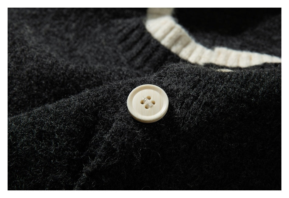Close-up of a cream four-hole button on a dark charcoal knit sweater near cream neckline trim.
