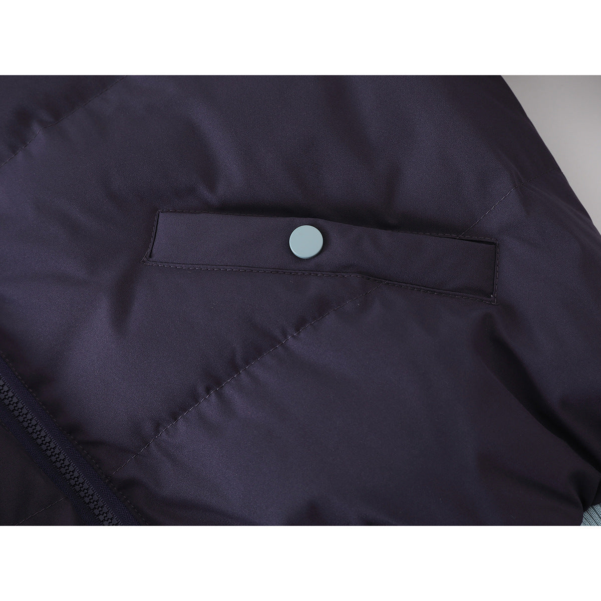 Close-up of a dark purple jacket pocket flap with a light blue snap and part of the front zipper.