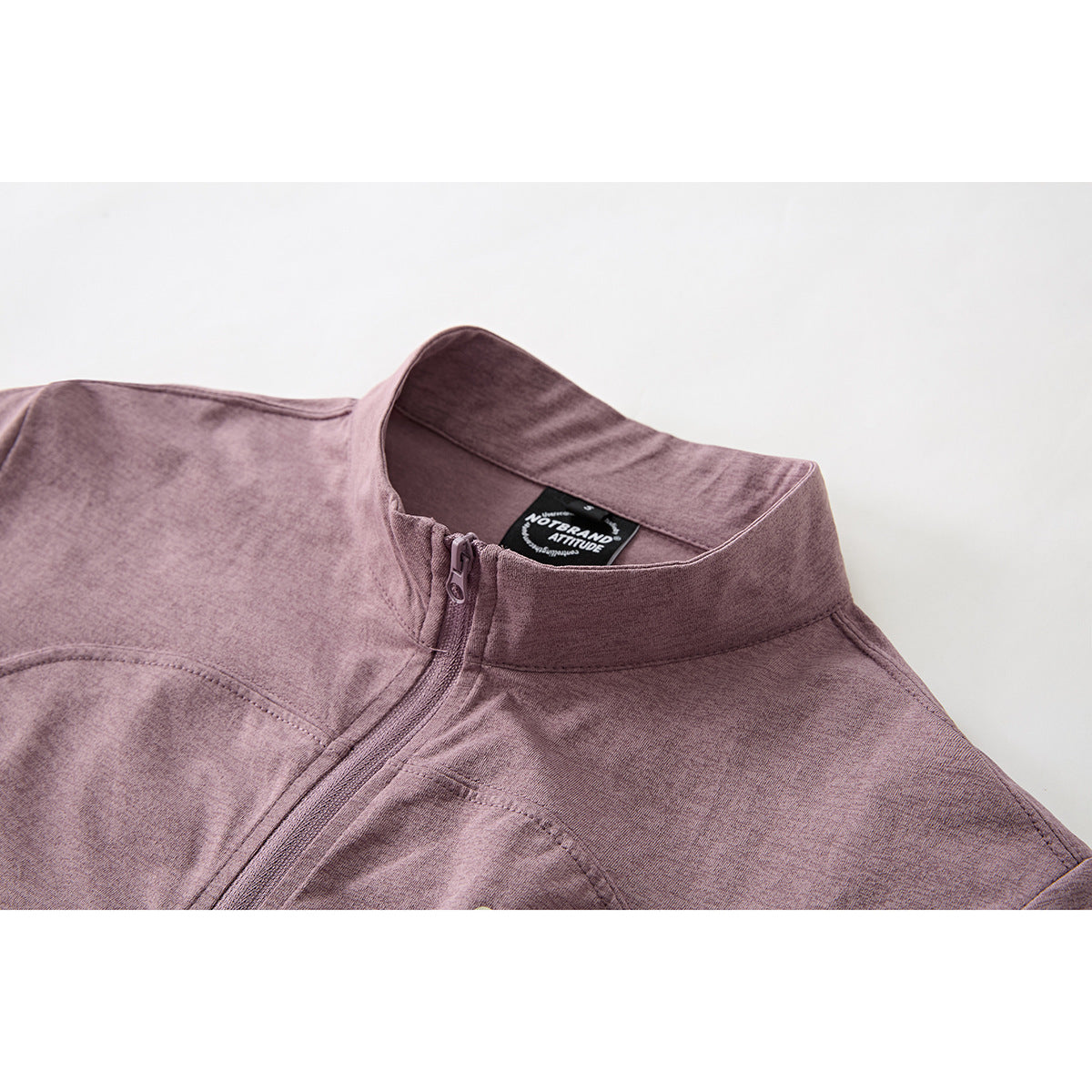 Close-up of a mauve short-sleeve zip top showing its stand collar, zipper, seams and inner neck label.