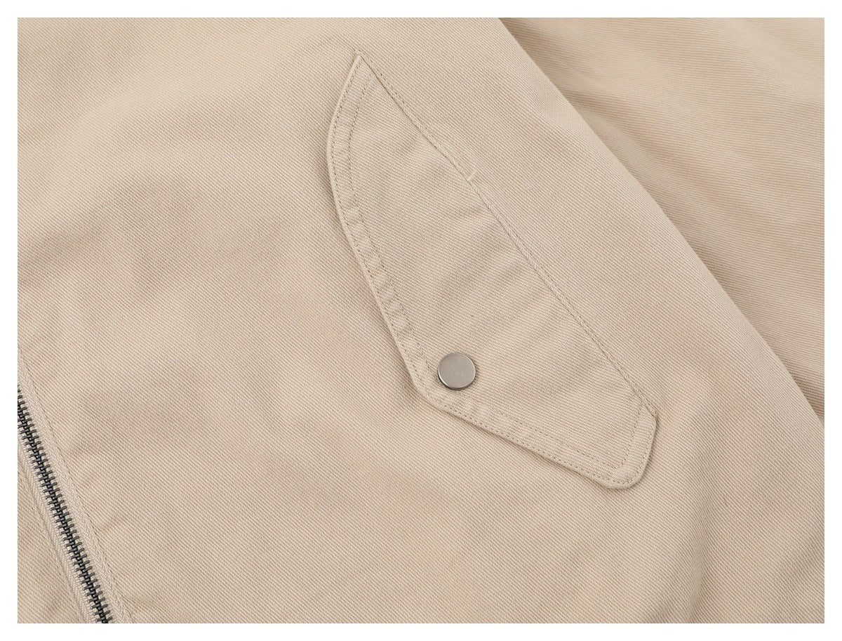 Close-up of a beige jacket pocket flap with a round metal snap and part of the front zipper.