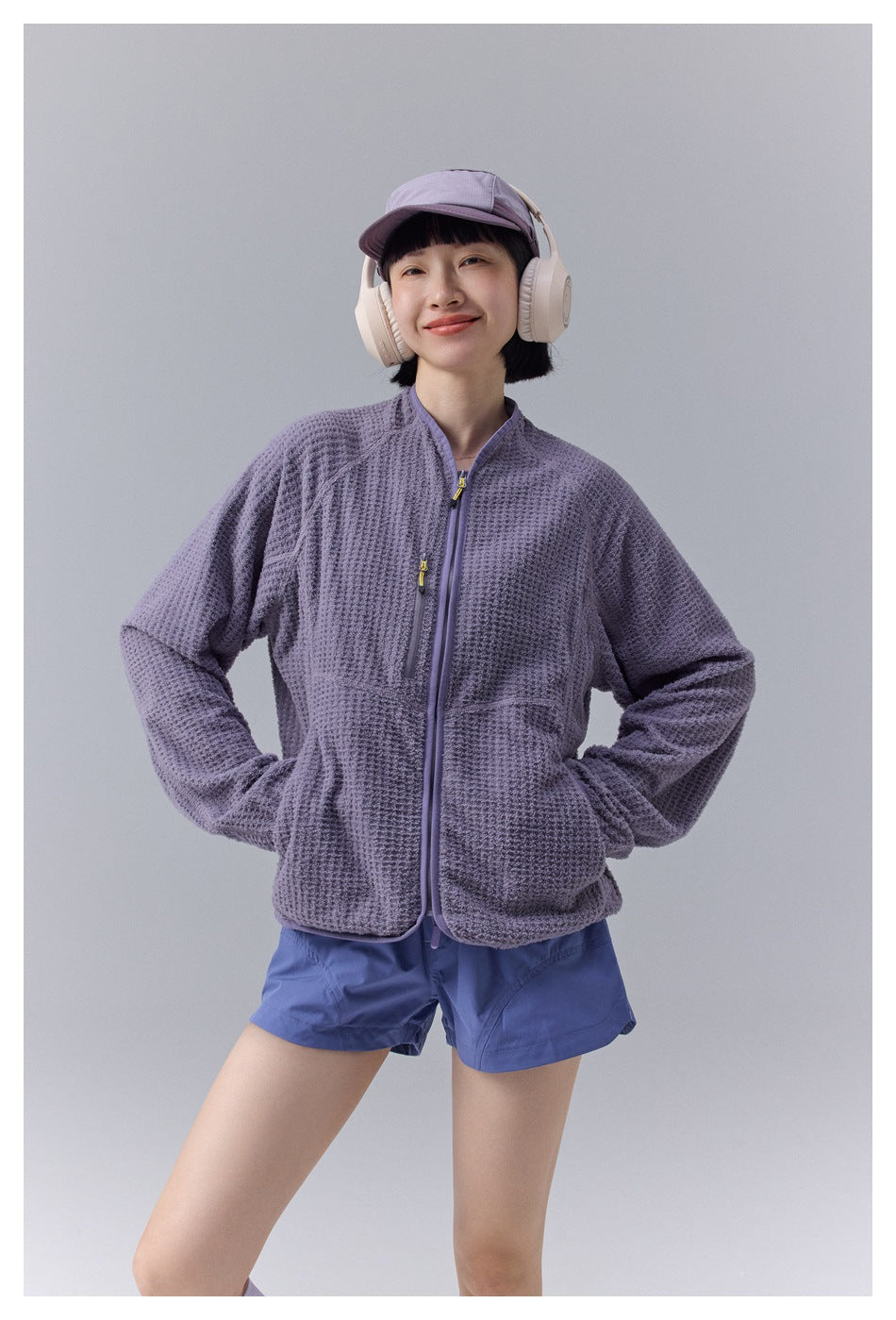 Closer front view of a model wearing a textured lavender zip jacket with front pockets and blue shorts.