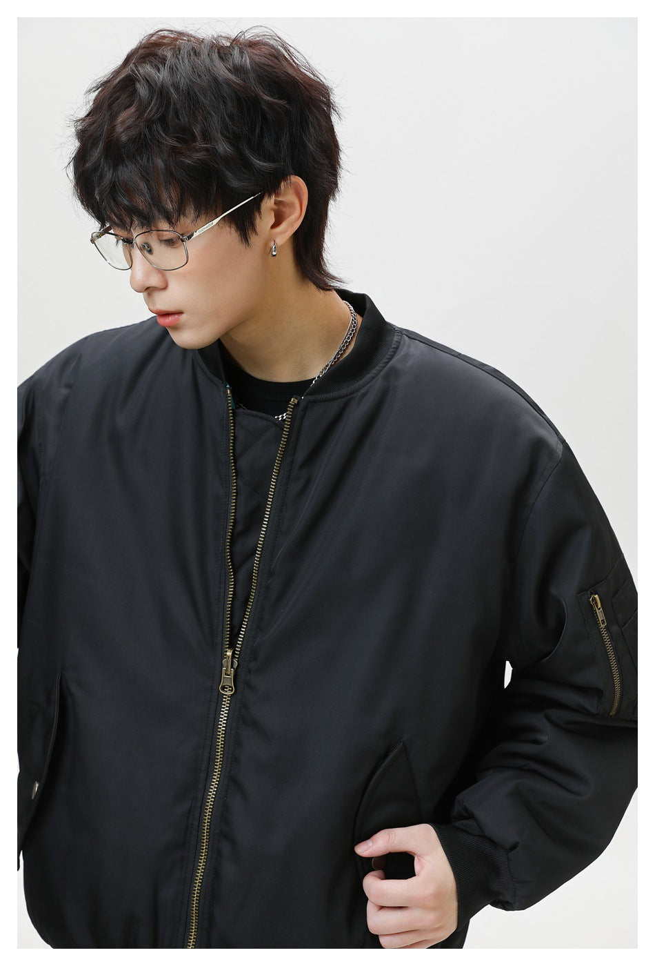 Close-up of a black bomber jacket on a model, showing its gold-tone front zipper and sleeve pocket.