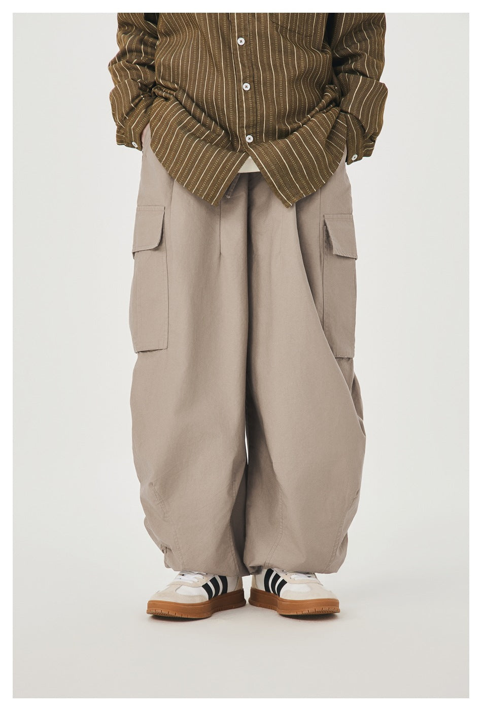 Model wearing taupe wide-leg cargo pants with flap pockets, striped olive shirt and sneakers, cropped at the torso