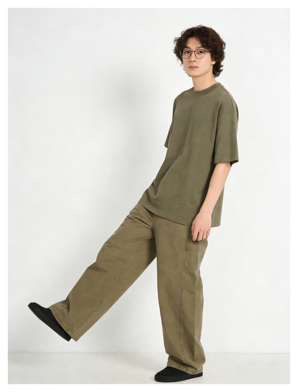 Model wearing an oversized olive short-sleeve T-shirt and loose olive-brown trousers, shown from the front.