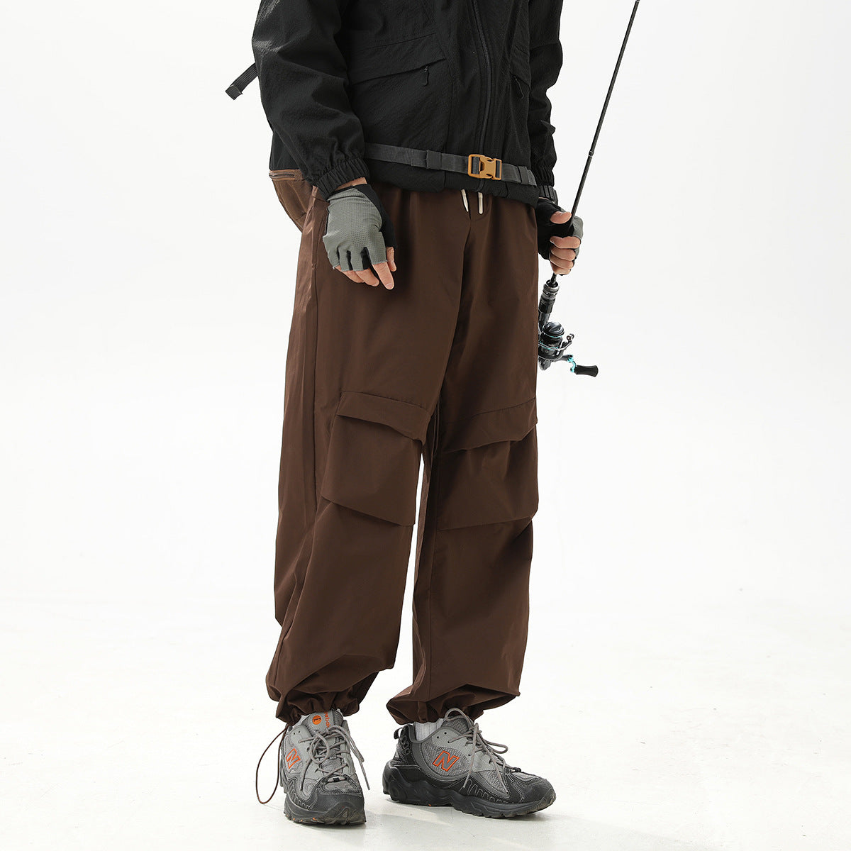 Cropped model wearing loose dark-brown cargo pants with layered pockets and an elasticized ankle hem.