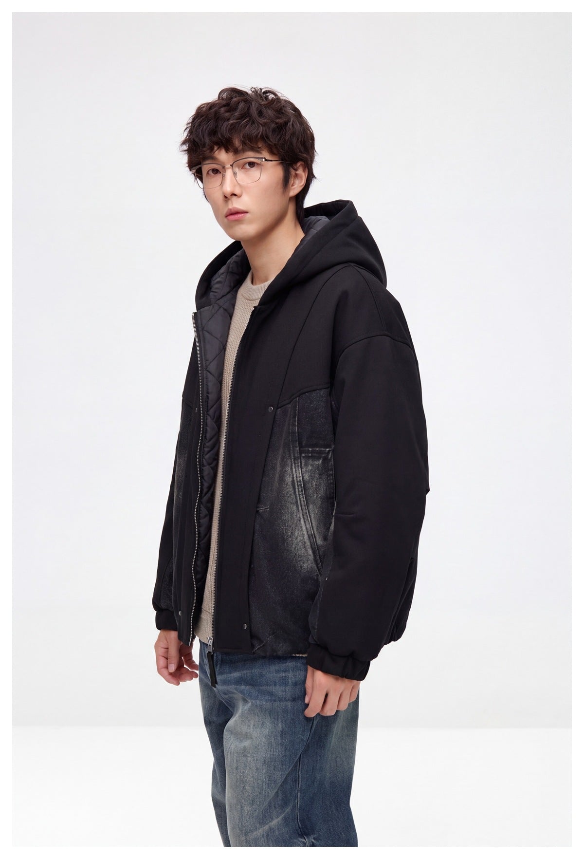 Man wearing the black hooded jacket partly unzipped, showing the quilted lining, three-quarter view