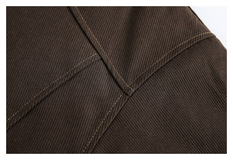Close-up of brown ribbed jacket fabric and intersecting seams with tan contrast stitching.