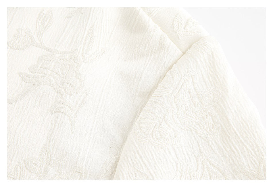 Close-up of ivory fabric showing raised floral motifs and a folded garment edge.