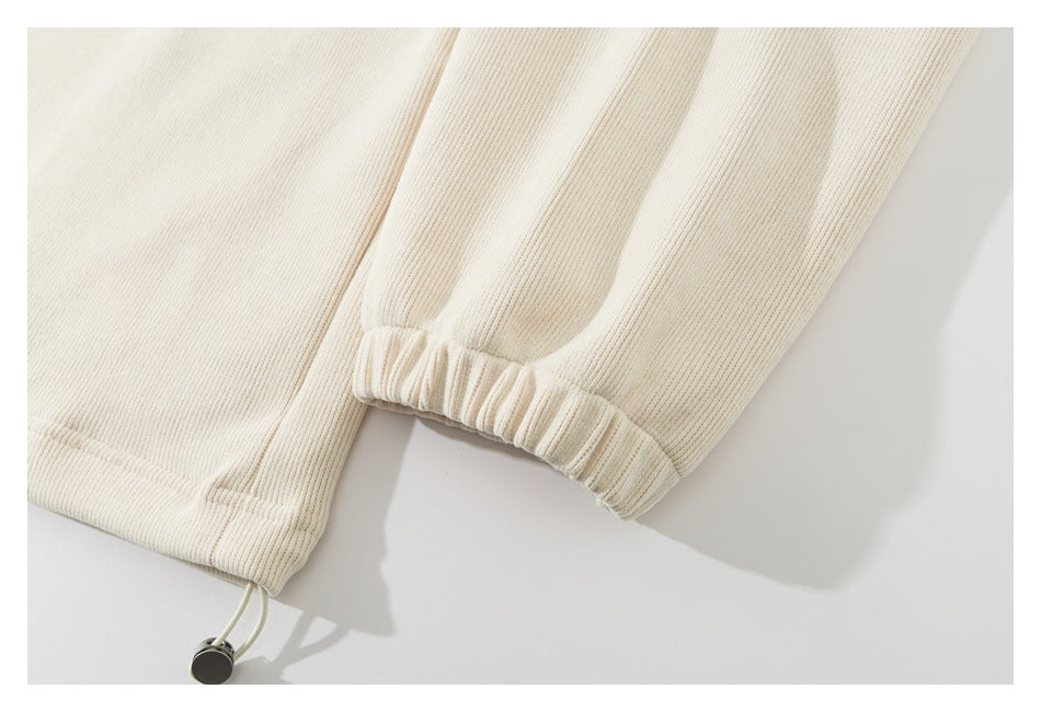 Close-up of an ivory ribbed garment showing a gathered sleeve cuff and adjustable drawstring hem.