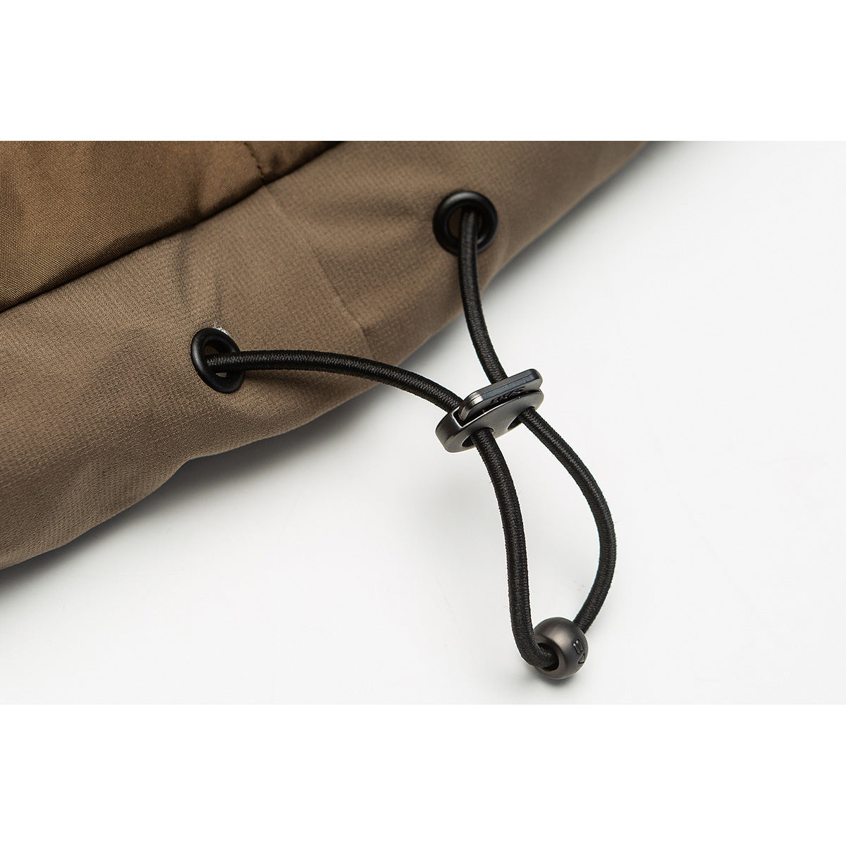 Close-up of a black adjustable drawcord and toggle at the hem of a brown jacket.