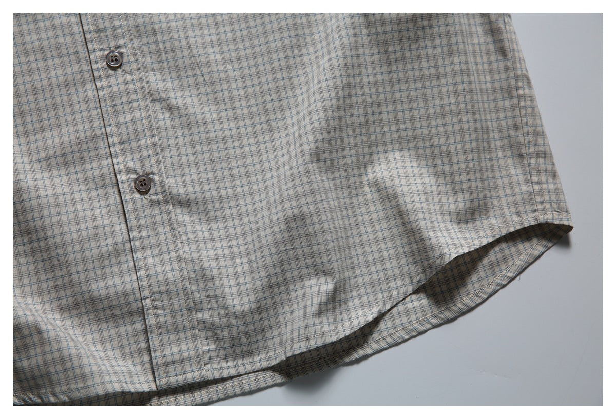 Close-up of a beige plaid shirt showing the button placket and curved hem.