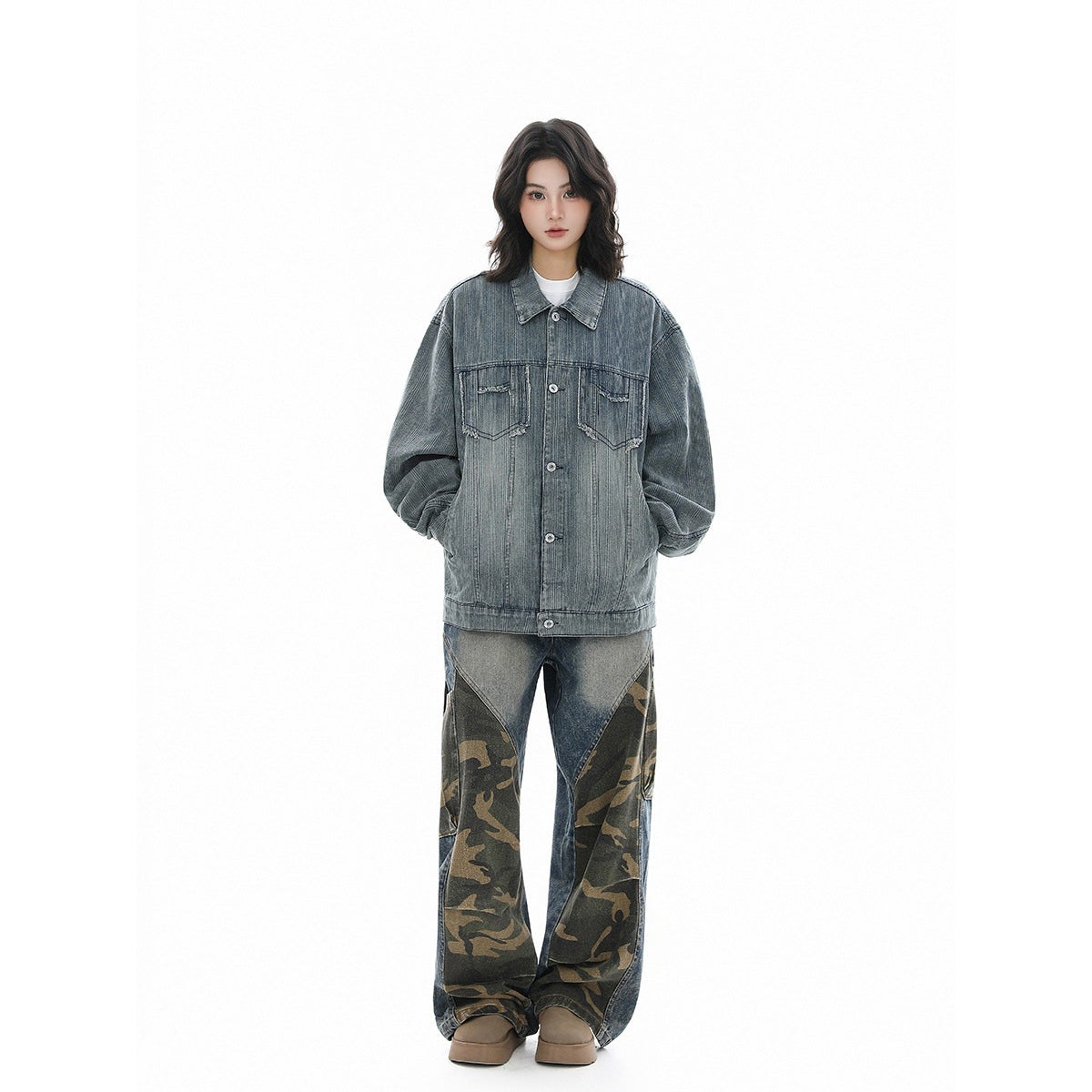 Full-length model wearing an oversized blue-gray denim jacket with distressed pockets and loose patchwork camouflage jeans.