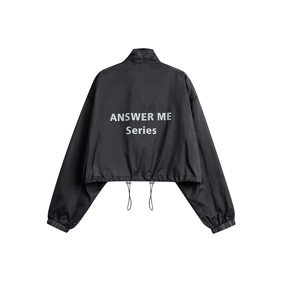 Back view of a black cropped jacket with elastic cuffs and hem, drawcords, and white “ANSWER ME Series” lettering.