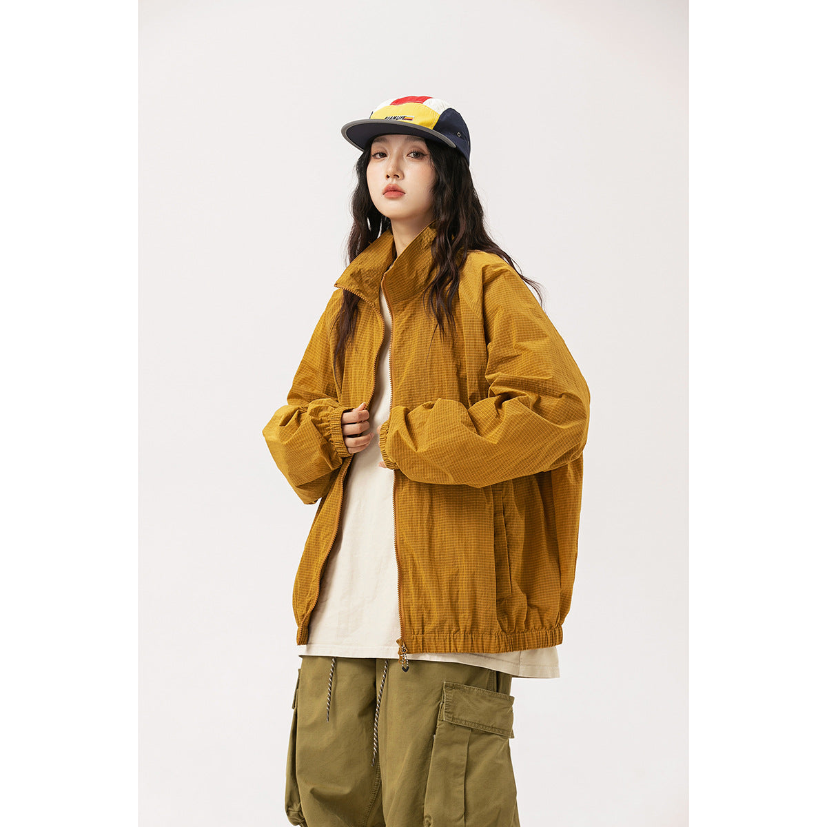 Model wearing an oversized mustard-gold zip jacket with a high collar and elastic cuffs and hem.