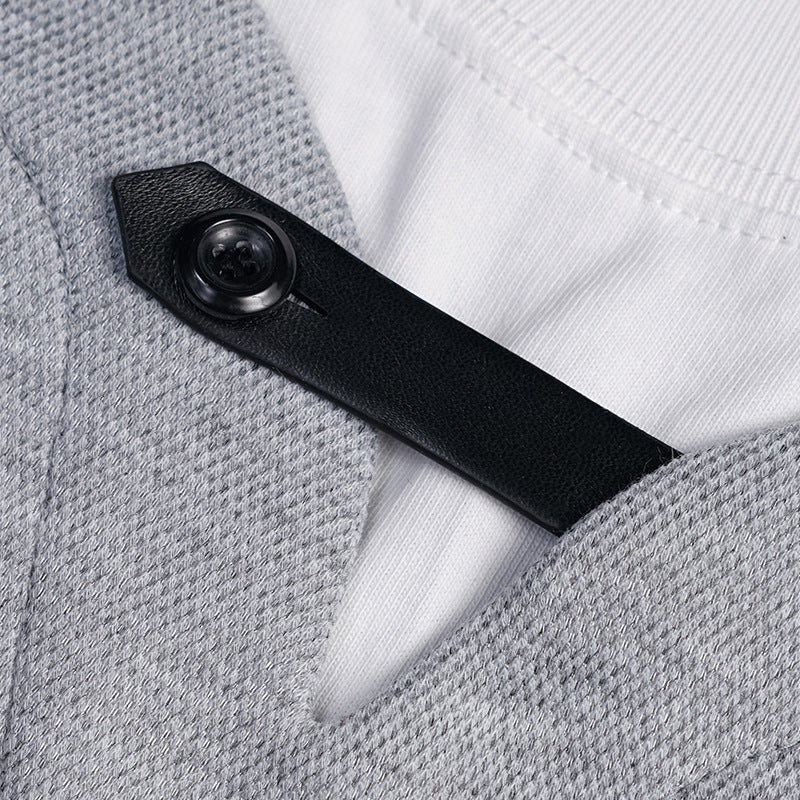 Close-up of a black buttoned tab fastening at the V-neck of a heather gray shirt over a white crewneck.