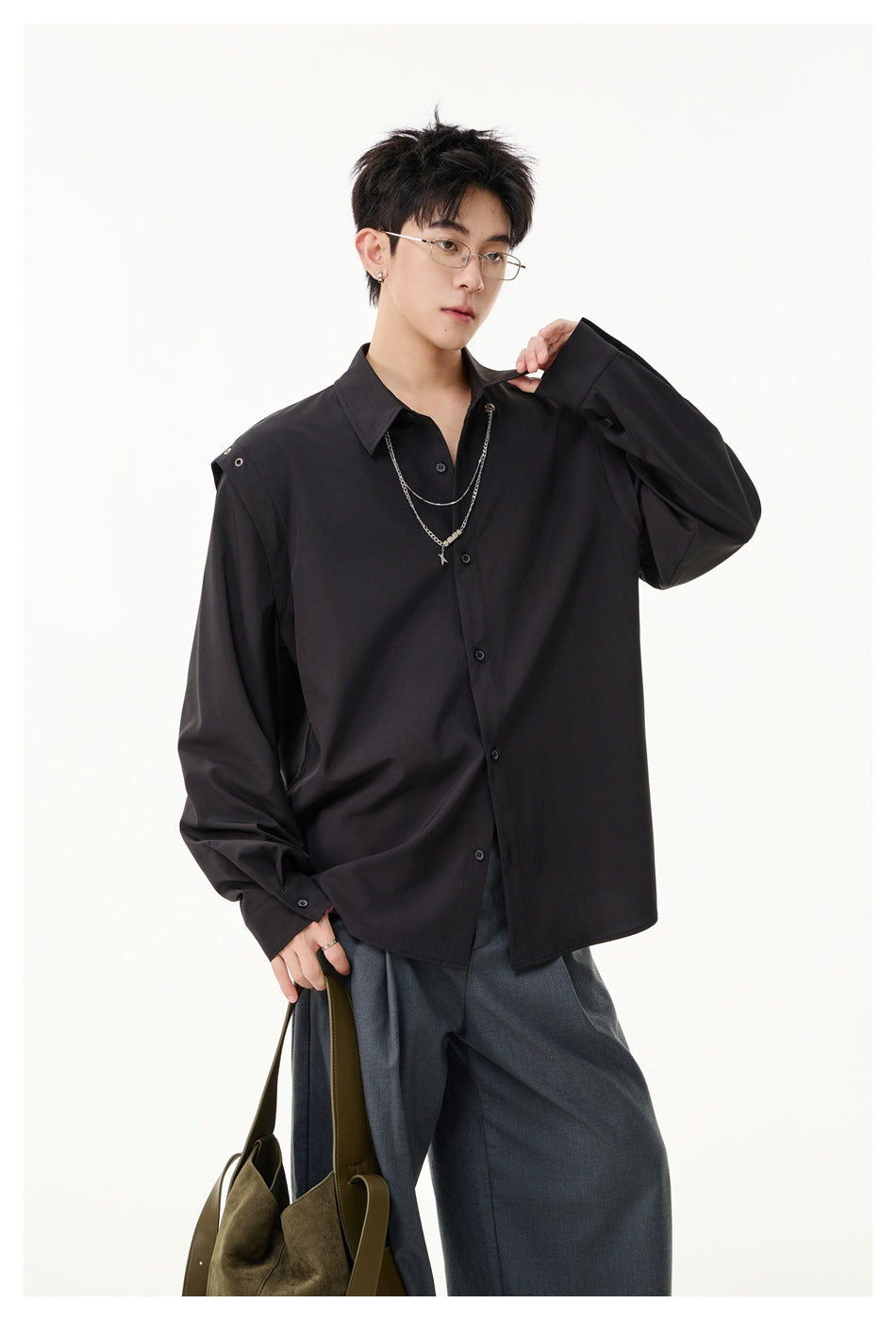 Model wearing a black oversized button-up shirt with shoulder snaps and silver chains, paired with gray trousers.