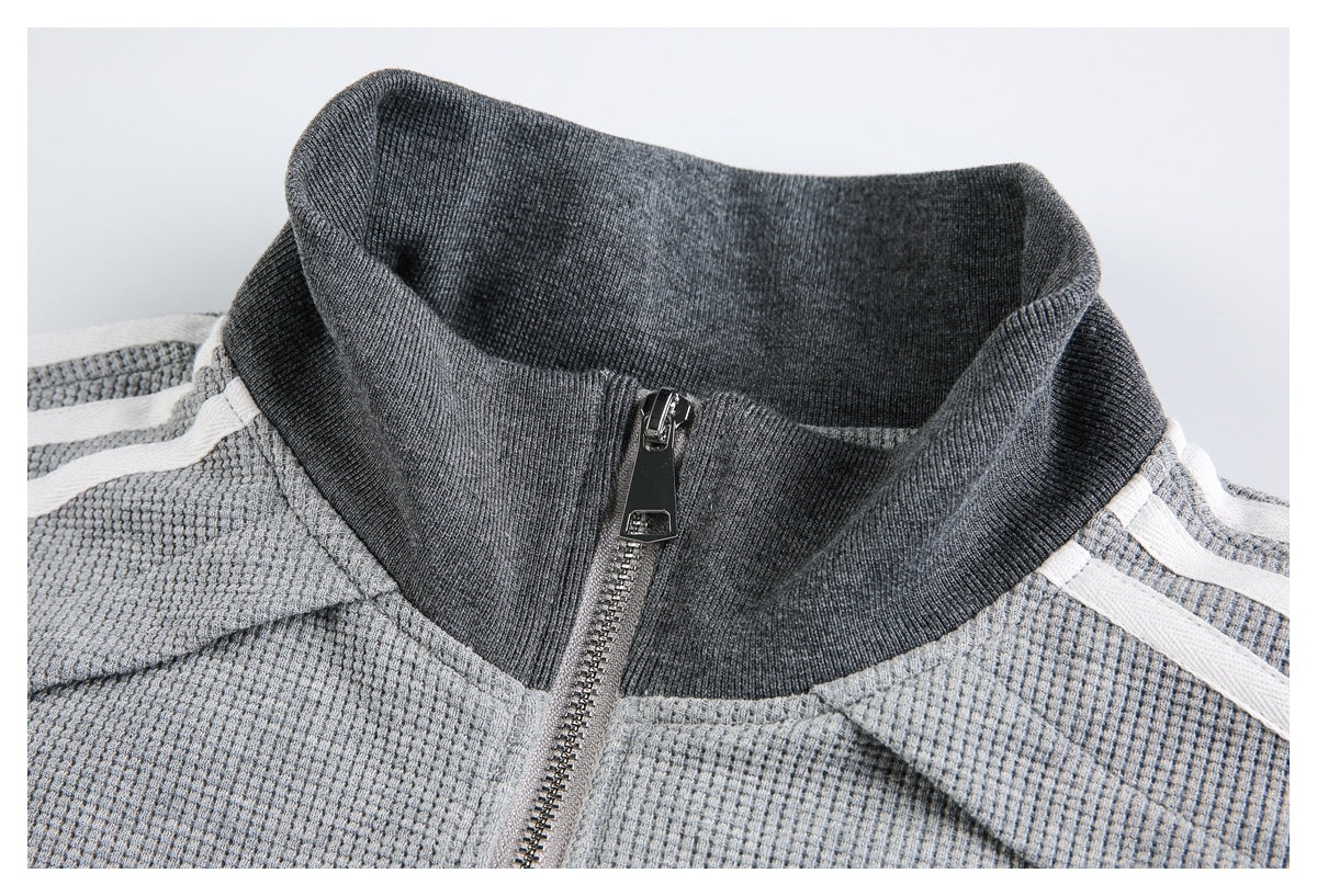 Close-up of a gray jacket's dark ribbed stand collar, front zipper, and white shoulder stripes.