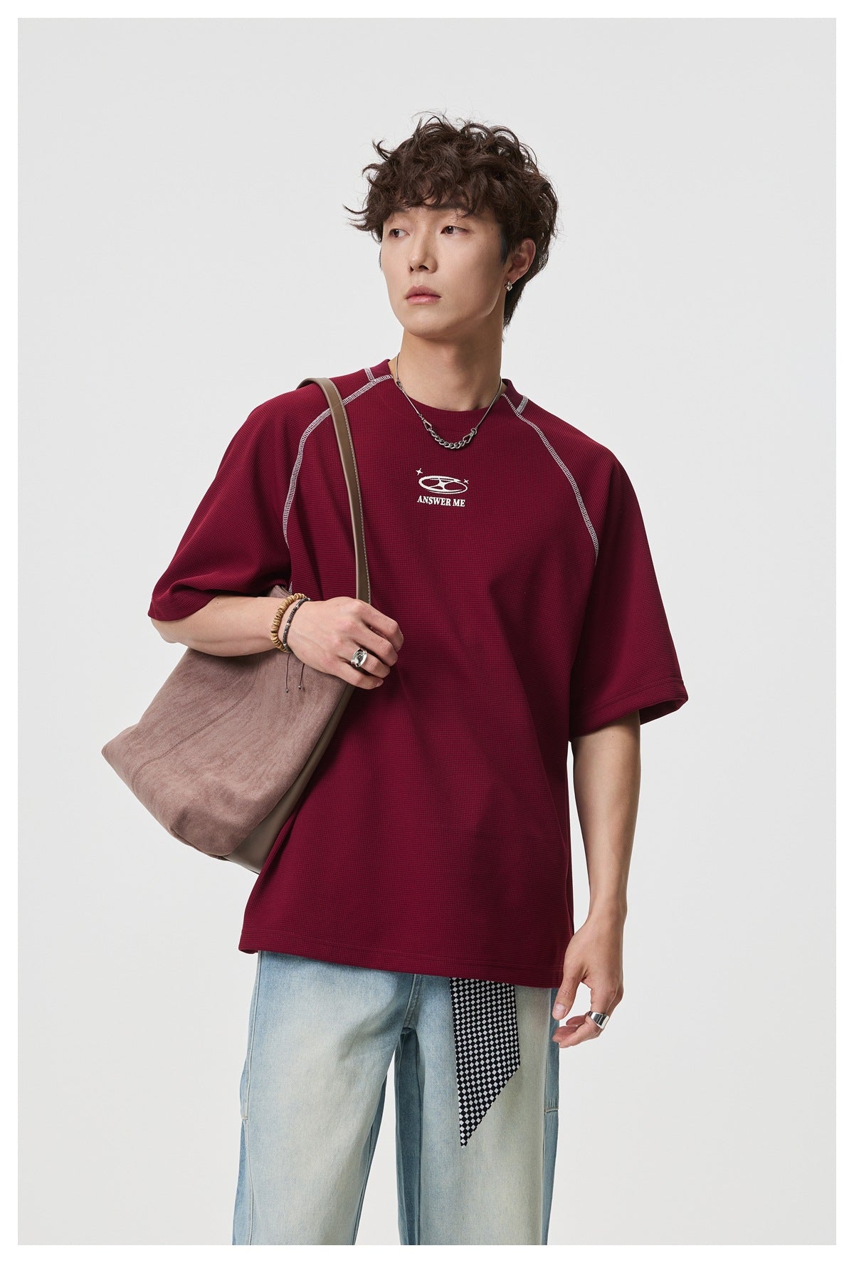 Model wearing a burgundy short-sleeve shirt with contrast seams and a small white chest graphic.
