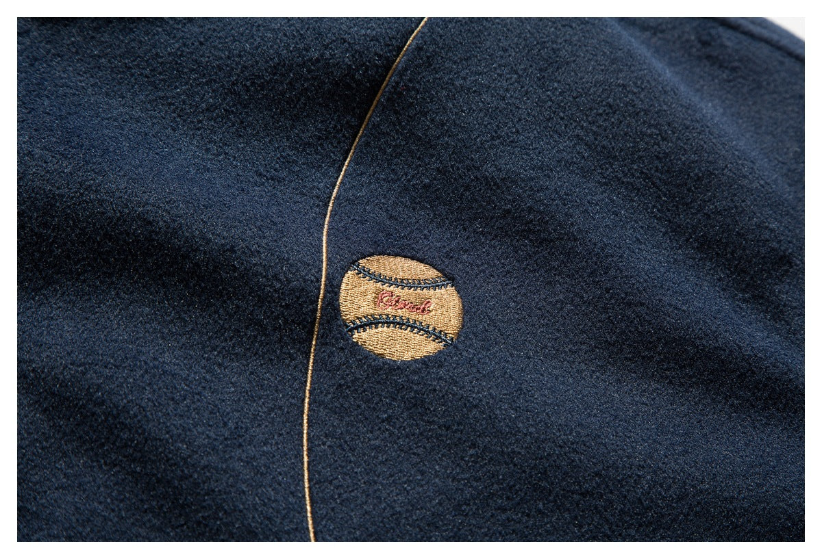 Close-up of a navy jacket chest with tan piping and a small embroidered baseball motif.