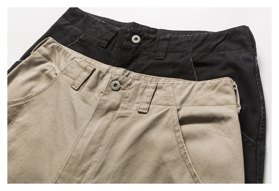 Close-up of black and beige trousers overlapping, showing their front waistbands, belt loops and metal buttons.