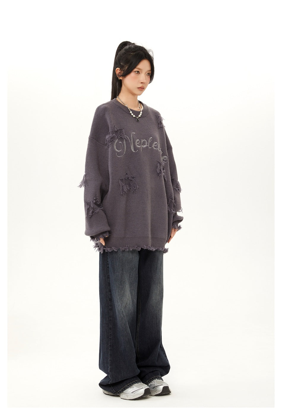 Model in side view wearing an oversized gray distressed knit sweater with wide-leg dark jeans and sneakers