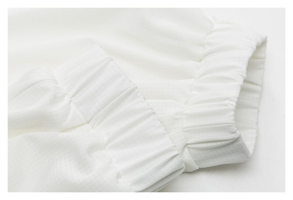 Close-up of a white garment's gathered, elasticized cuff with subtle grid-textured fabric.