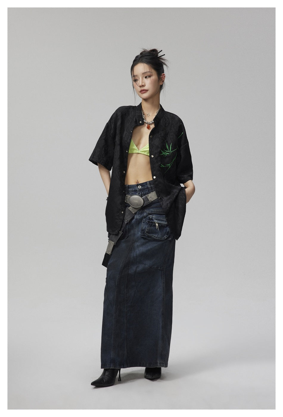Model wearing an open black patterned shirt with green branch embroidery and short sleeves.
