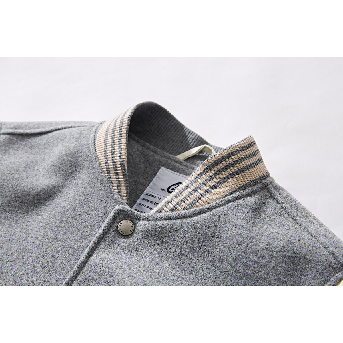 Close-up of a gray jacket collar with cream and charcoal striped ribbing, a snap, and an inner label.