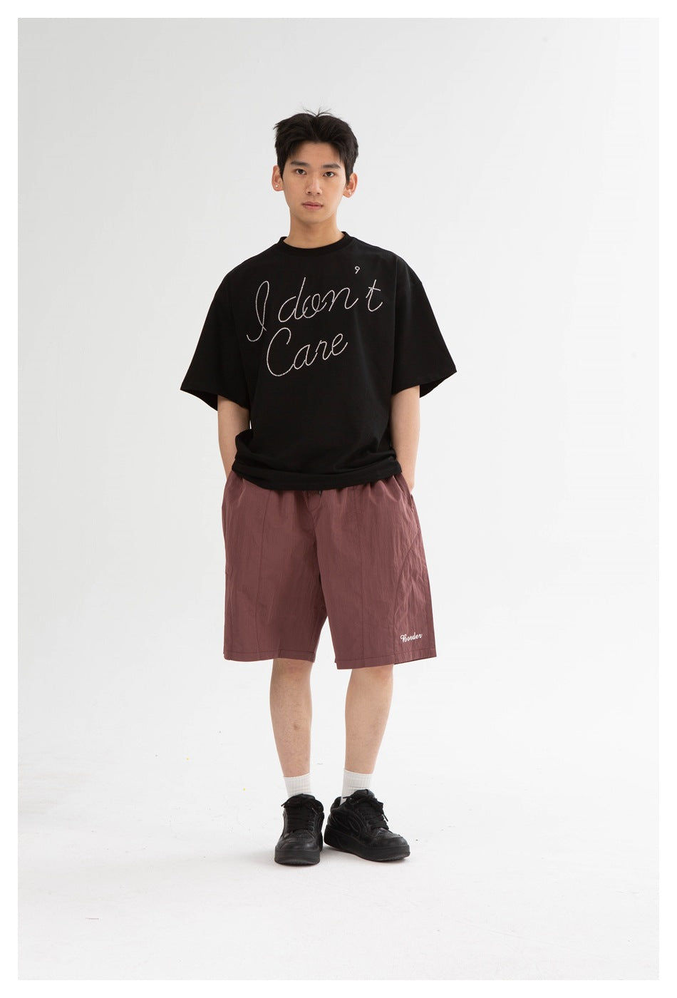Front view of a model wearing mauve knee-length shorts and a black T-shirt with white script.