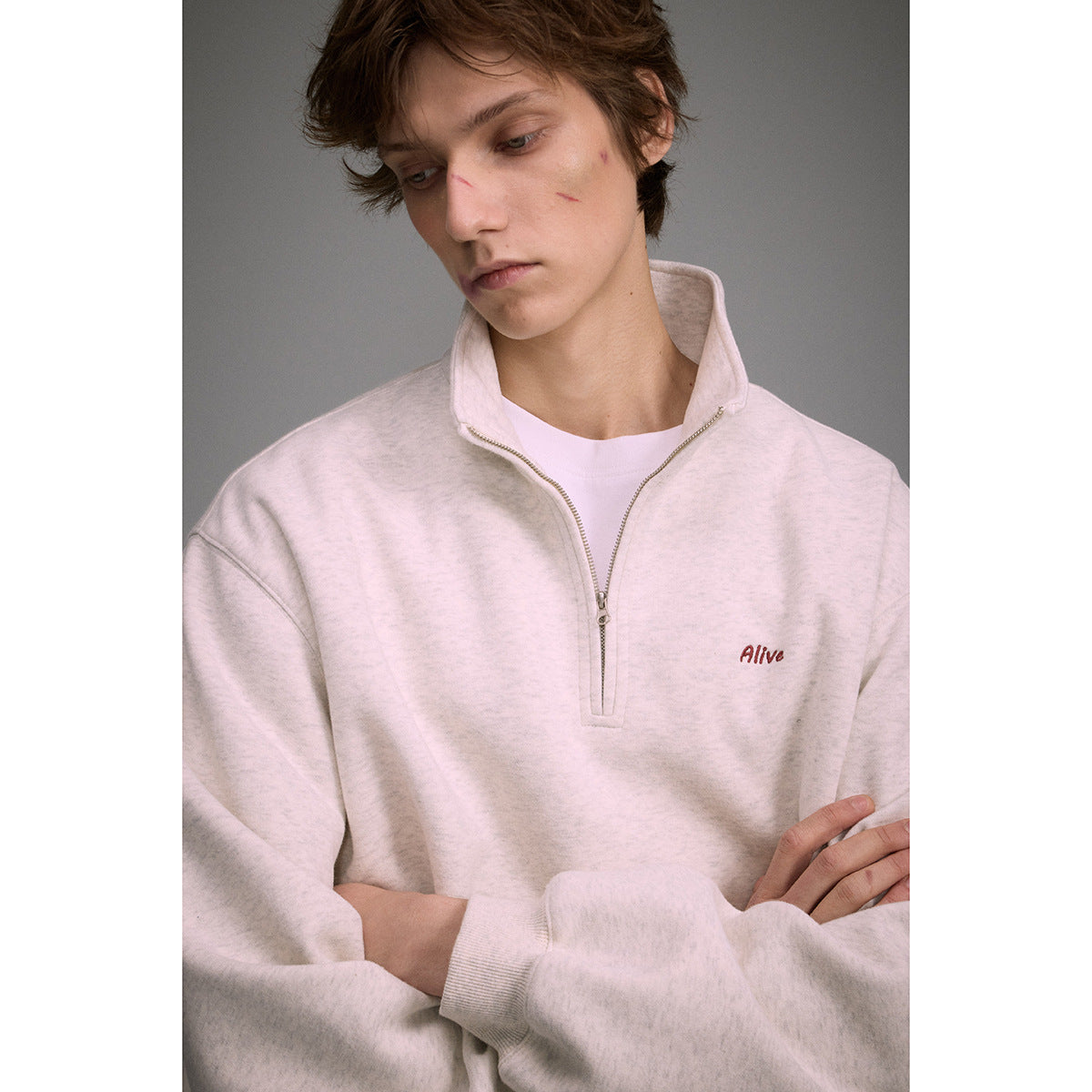 Close-up of a model wearing a light oatmeal quarter-zip sweatshirt with a raised collar and small chest embroidery.