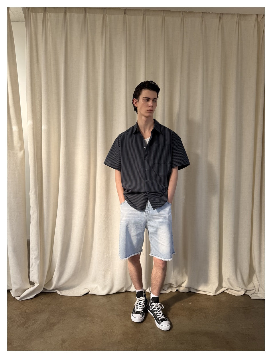 Front view of a model wearing a black pinstriped short-sleeve shirt with a chest pocket and light denim shorts.