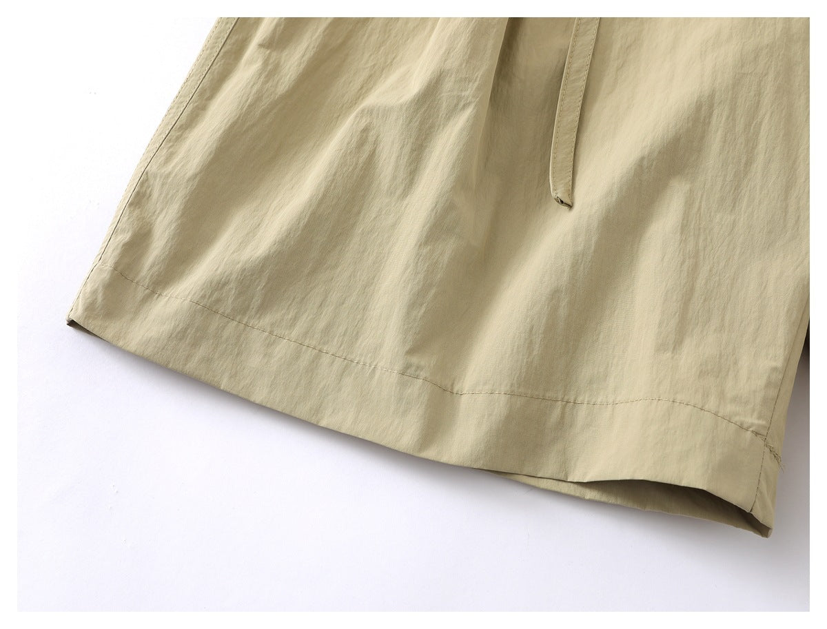 Close-up of the beige shorts' hem, stitching and a narrow hanging belt end.