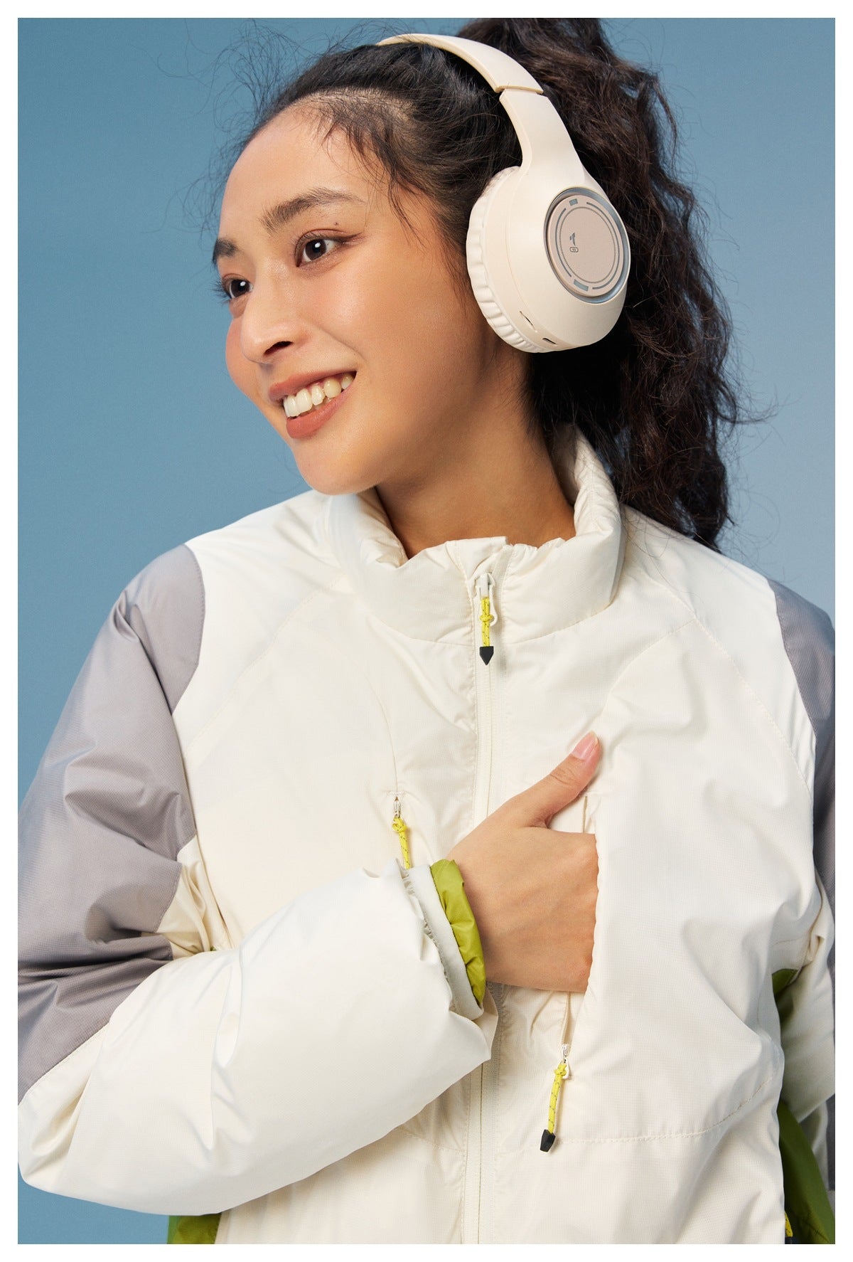 Close view of a woman wearing a white high-collar zip jacket with gray sleeves, lime accents, and yellow zipper pulls.