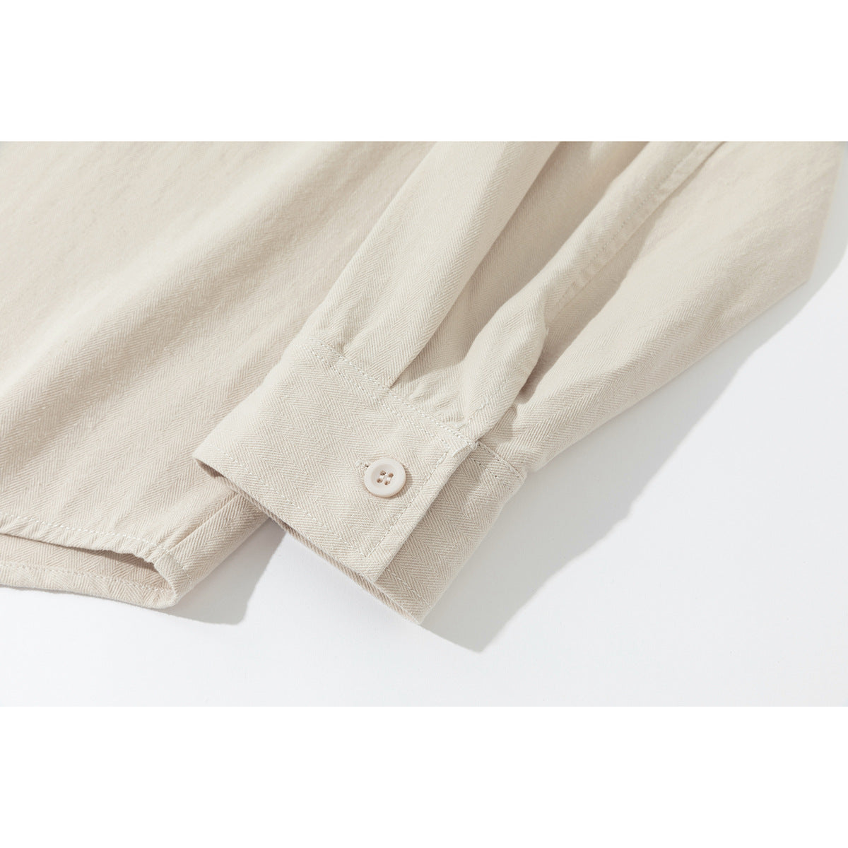 Close-up of the cream herringbone shirt's long sleeve and buttoned cuff.