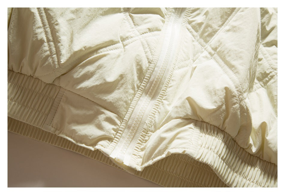 Close-up of an ivory quilted jacket's zipper, stitched panels, and gathered elastic hem.