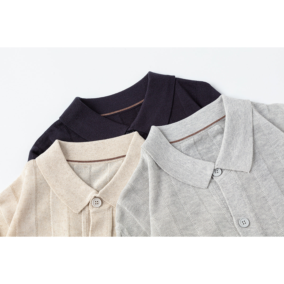 Close-up of three ribbed knit collared shirts in cream, light gray, and navy.