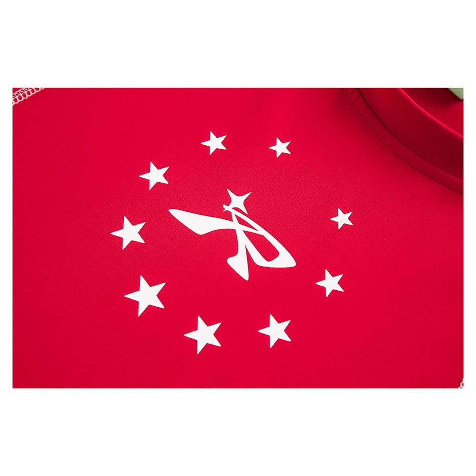Close-up of the shirt’s white star-and-emblem print on bright red fabric, with the neckline partly visible.