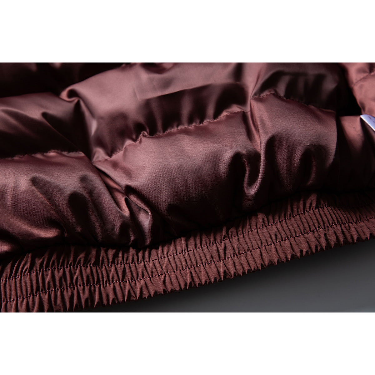 Close-up of the burgundy jacket's gathered elastic hem and stitched panels.