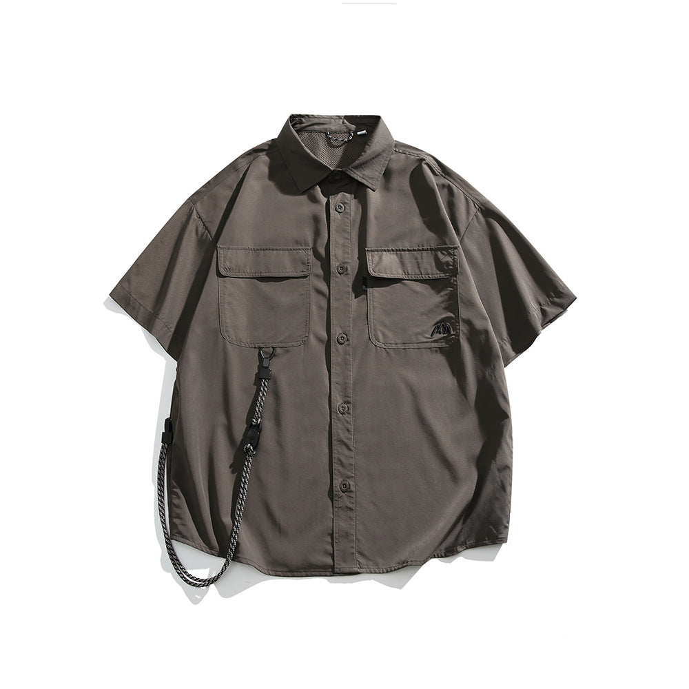 Brown short-sleeve button-up shirt with two flap chest pockets, tonal logo and a hanging cord, flat lay front view