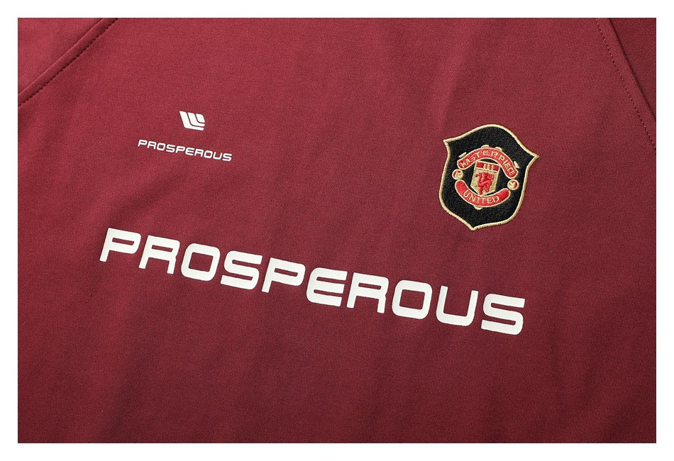 Front chest close-up showing a small crest and white “PROSPEROUS” lettering on burgundy fabric.