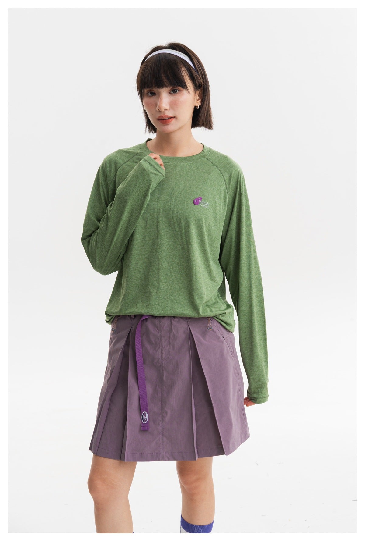 Closer view of a model wearing a green long-sleeve shirt and lavender pleated skirt.