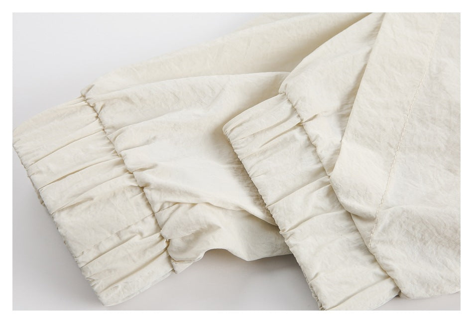 Close-up of cream garment fabric with a gathered elastic edge and stitched panel seams.