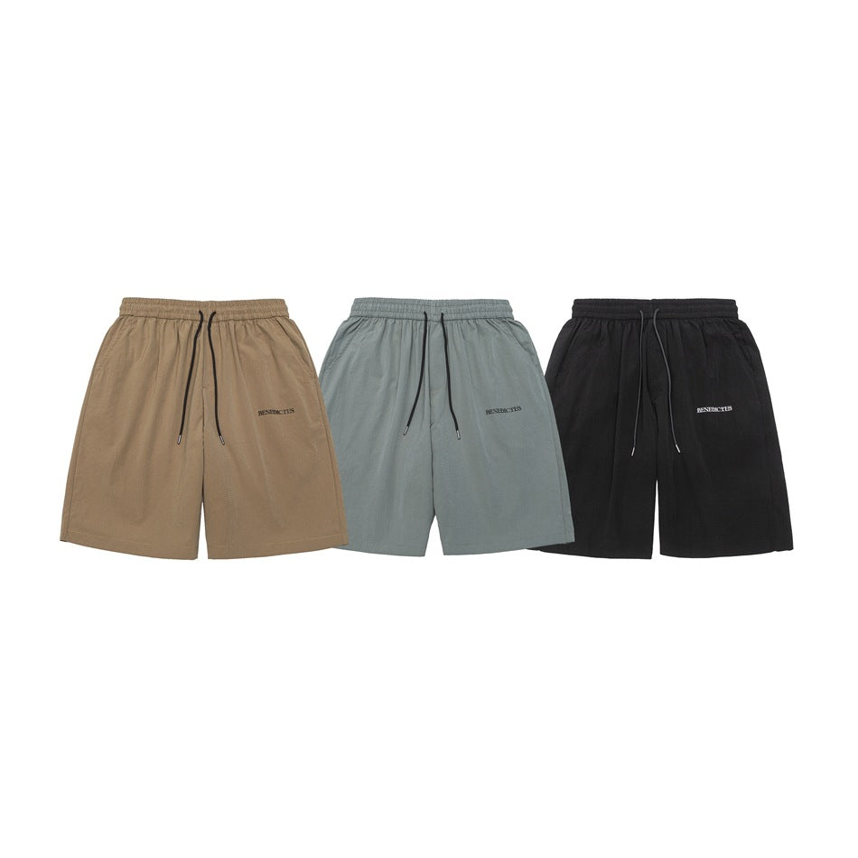 Three pairs of loose shorts shown from the front in tan, gray-green, and black, with elastic waists and drawstrings.