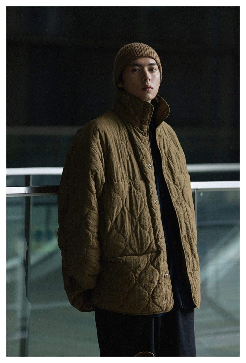 Model wearing an olive-brown quilted coat with a high buttoned collar and rounded diamond quilting.
