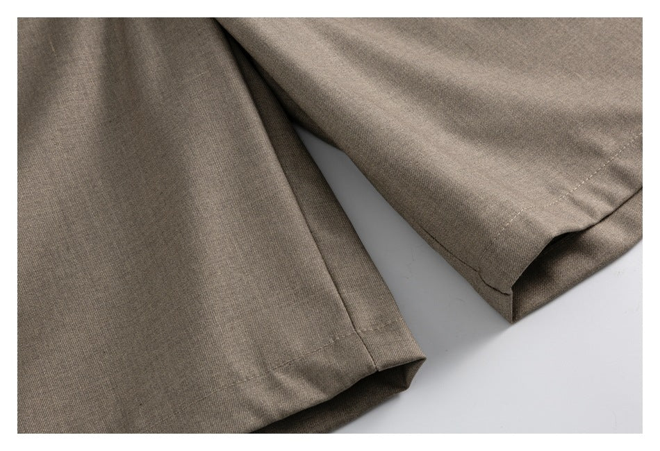 Close-up of the stitched hems on taupe-brown trouser legs.